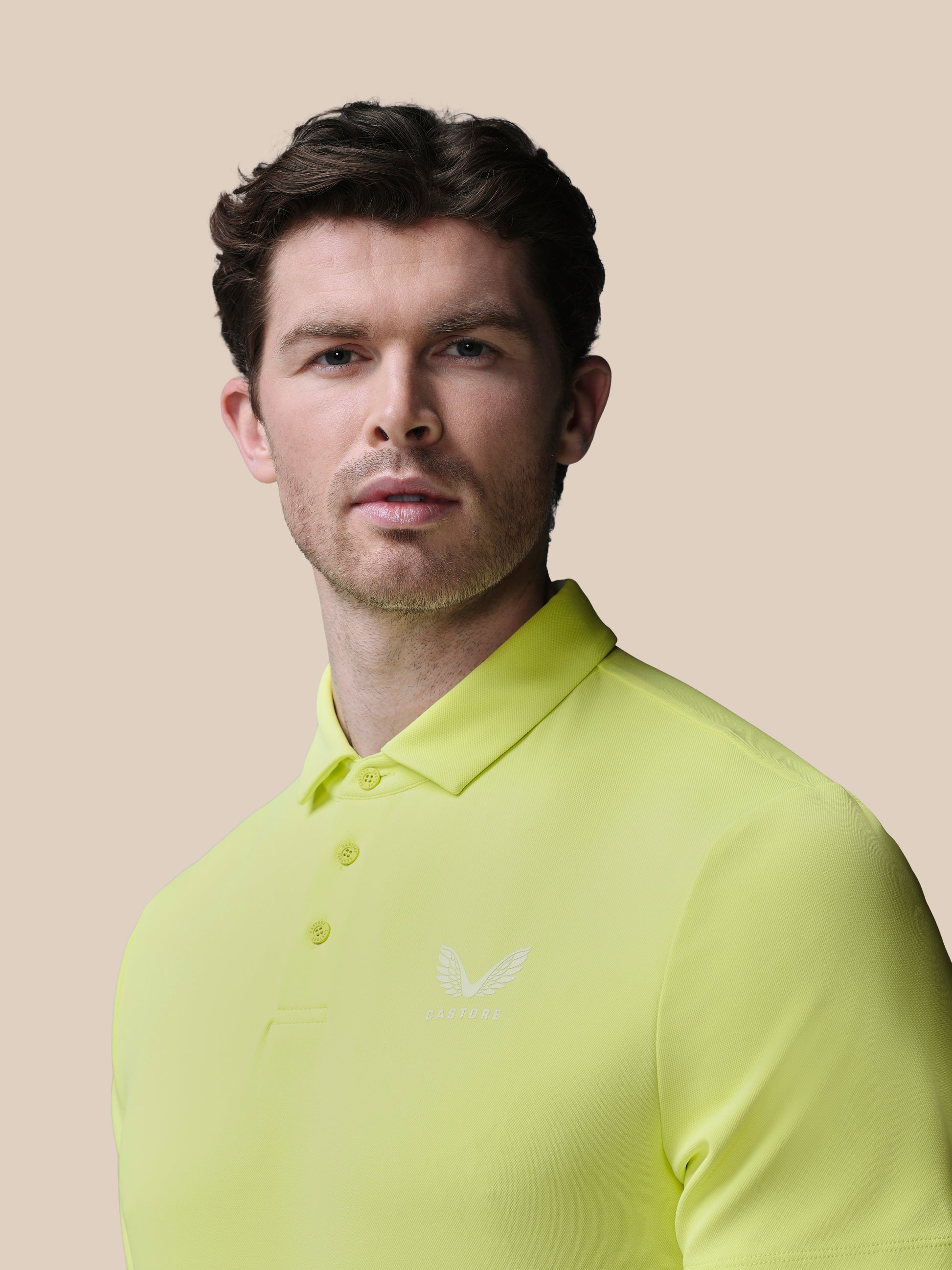 Man wearing a bright yellow polo shirt with the Castore logo on a beige background