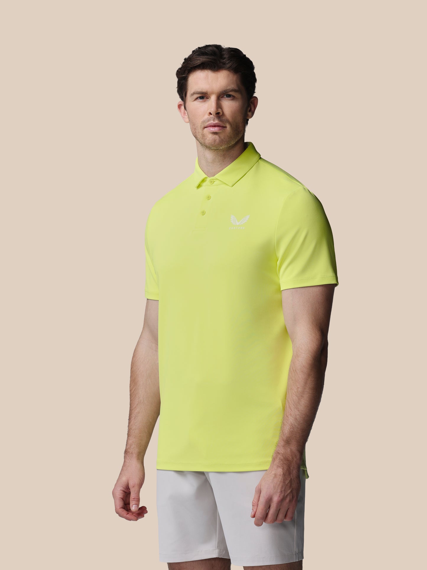 Man wearing a bright yellow polo shirt and white shorts on a beige background