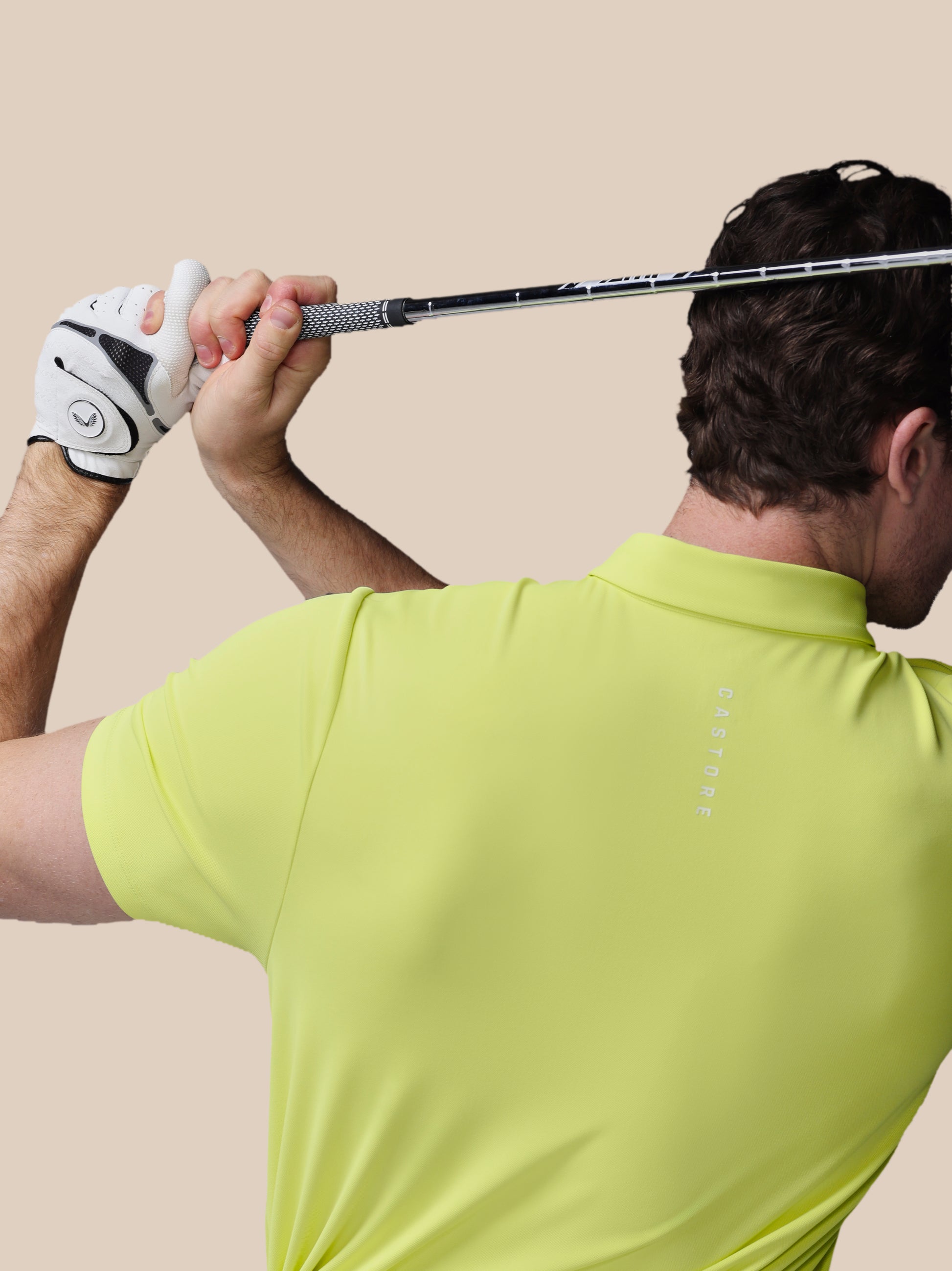 Man in a yellow shirt holding a golf club against a beige background