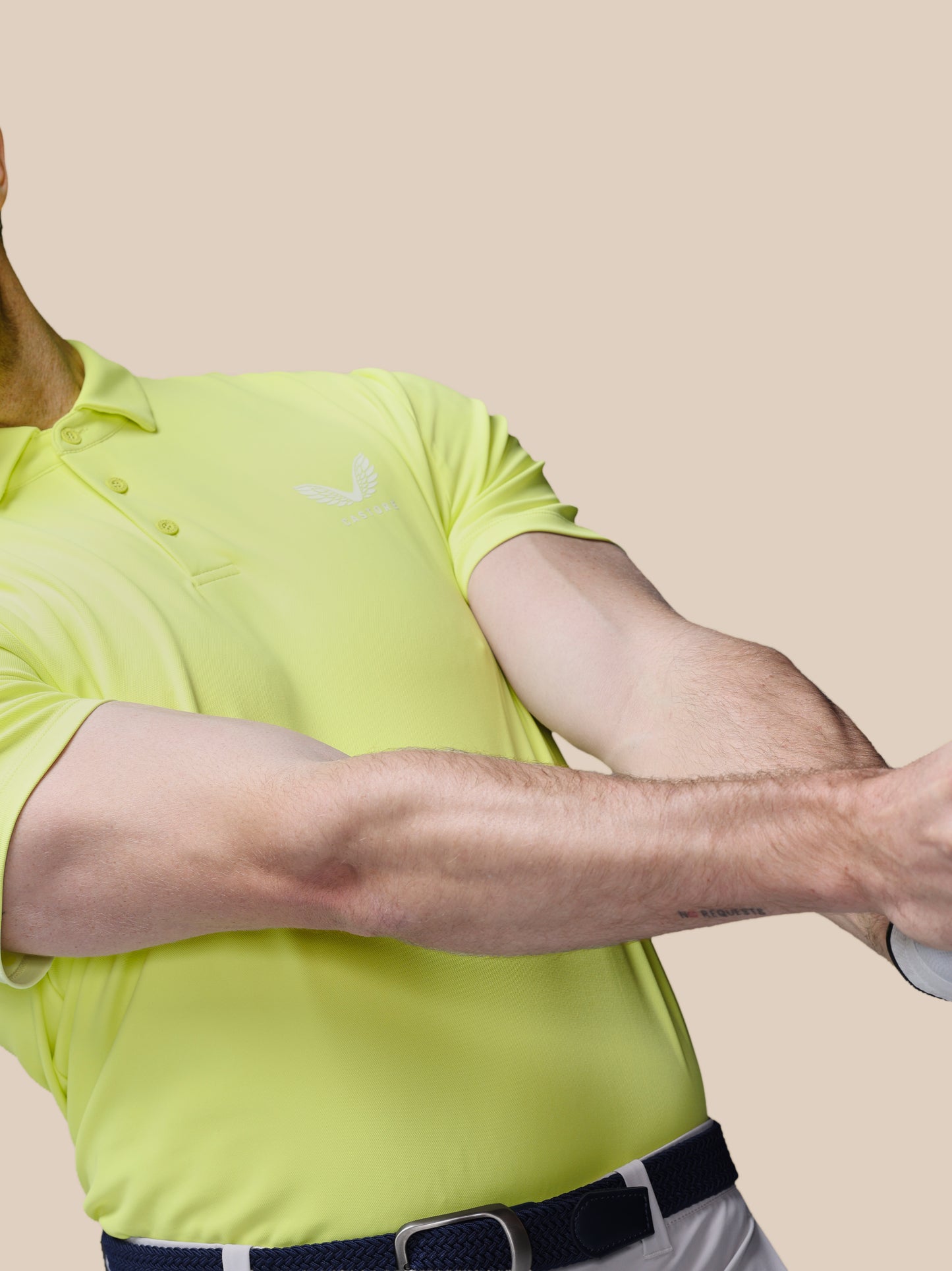 Person wearing a bright yellow golf shirt with the Castore logo on a beige background