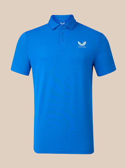 A bright blue short-sleeve polo shirt with a small white embroidered wing logo and the word 'CASTORE' on the left chest, displayed on a solid beige background.