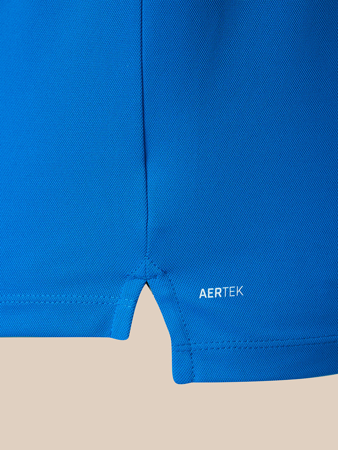 Close-up of a bright blue athletic garment showing the hem and a small white AERTEK logo on a light beige background.