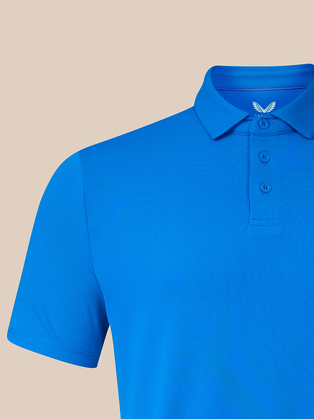 A bright blue short-sleeve polo shirt shown on a mannequin torso against a solid beige background. The shirt features a classic collar, three-button placket, and a small white embroidered wing logo on the inner neck label.