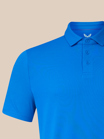 A bright blue short-sleeve polo shirt shown on a mannequin torso against a solid beige background. The shirt features a classic collar, three-button placket, and a small white embroidered wing logo on the inner neck label.