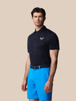 Man wearing a navy polo shirt and blue shorts on a beige background