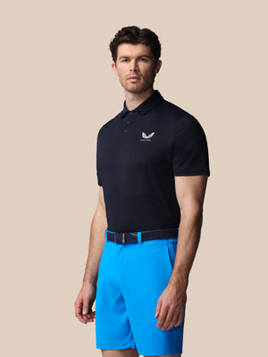 Man wearing a navy polo shirt and blue shorts on a beige background