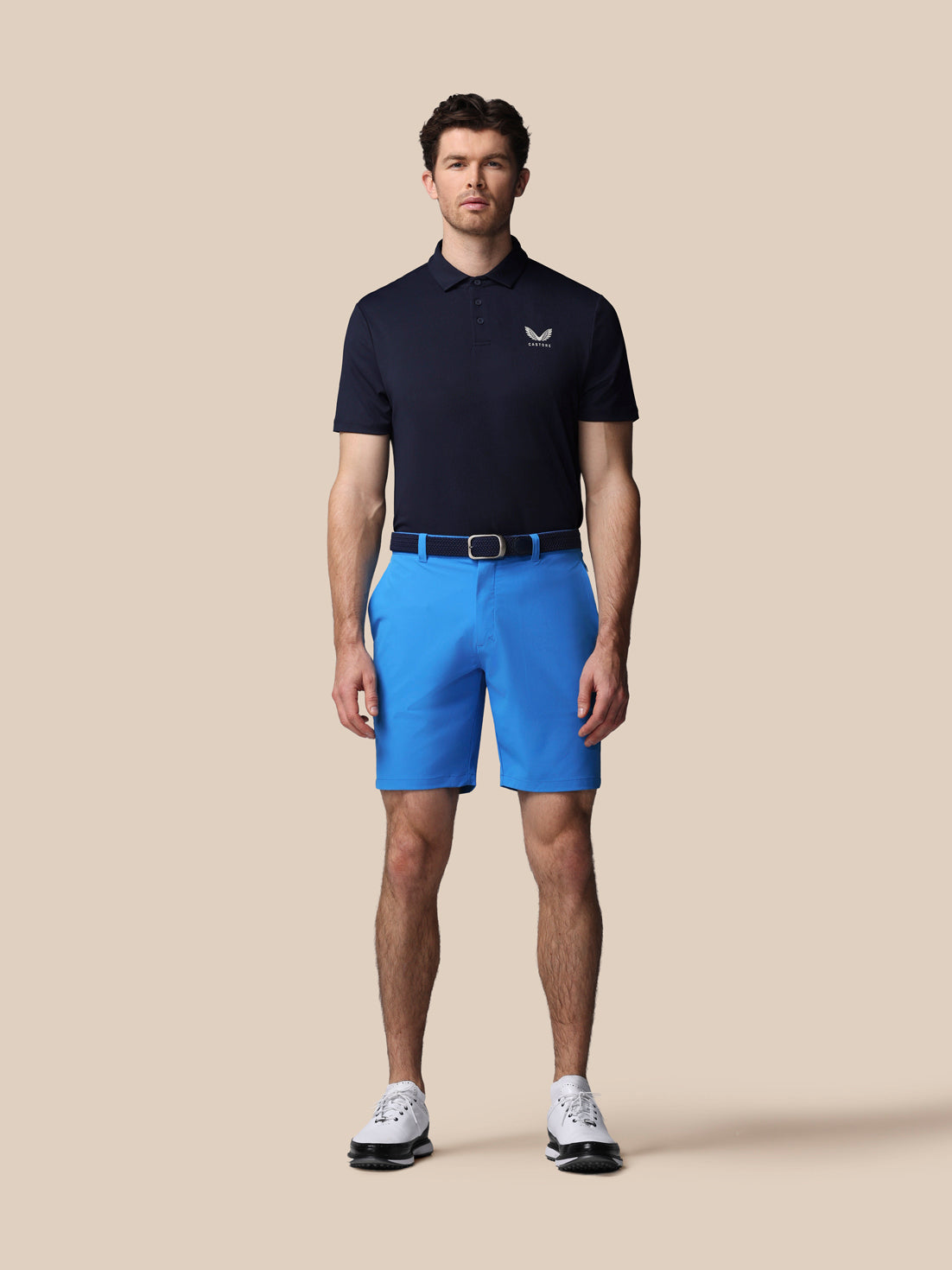 Man wearing a navy polo shirt and blue shorts on a beige background