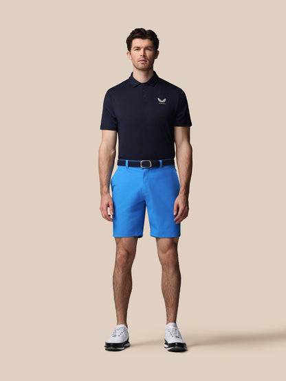 Man wearing a navy polo shirt and blue shorts on a beige background