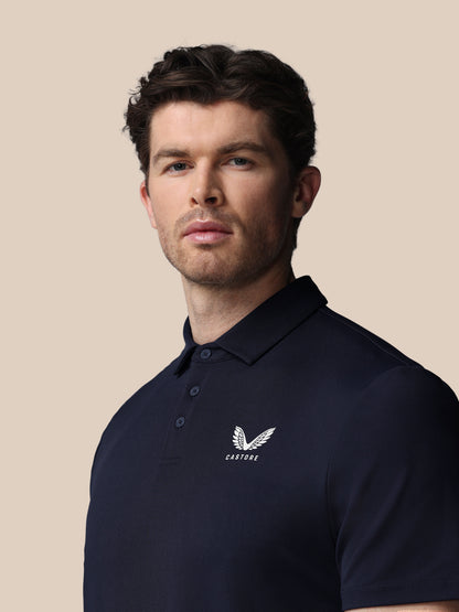 Man wearing a navy polo shirt with a Castore logo on a beige background