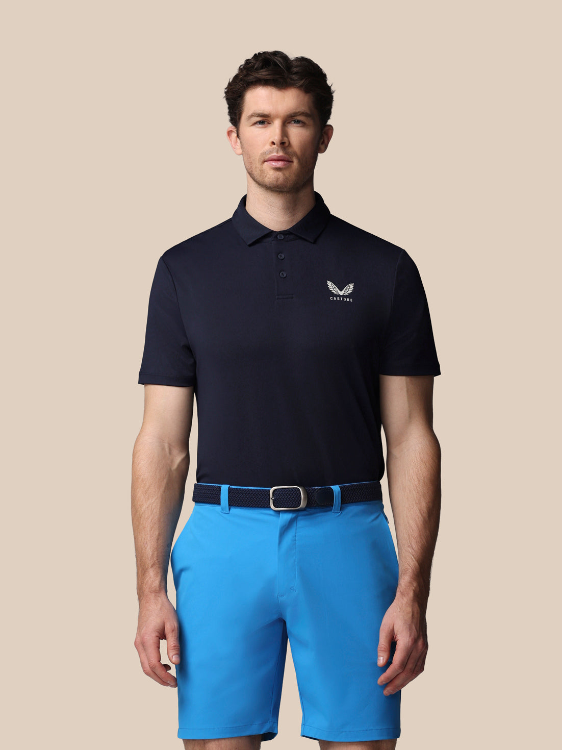 Man wearing a navy polo shirt and blue shorts on a beige background