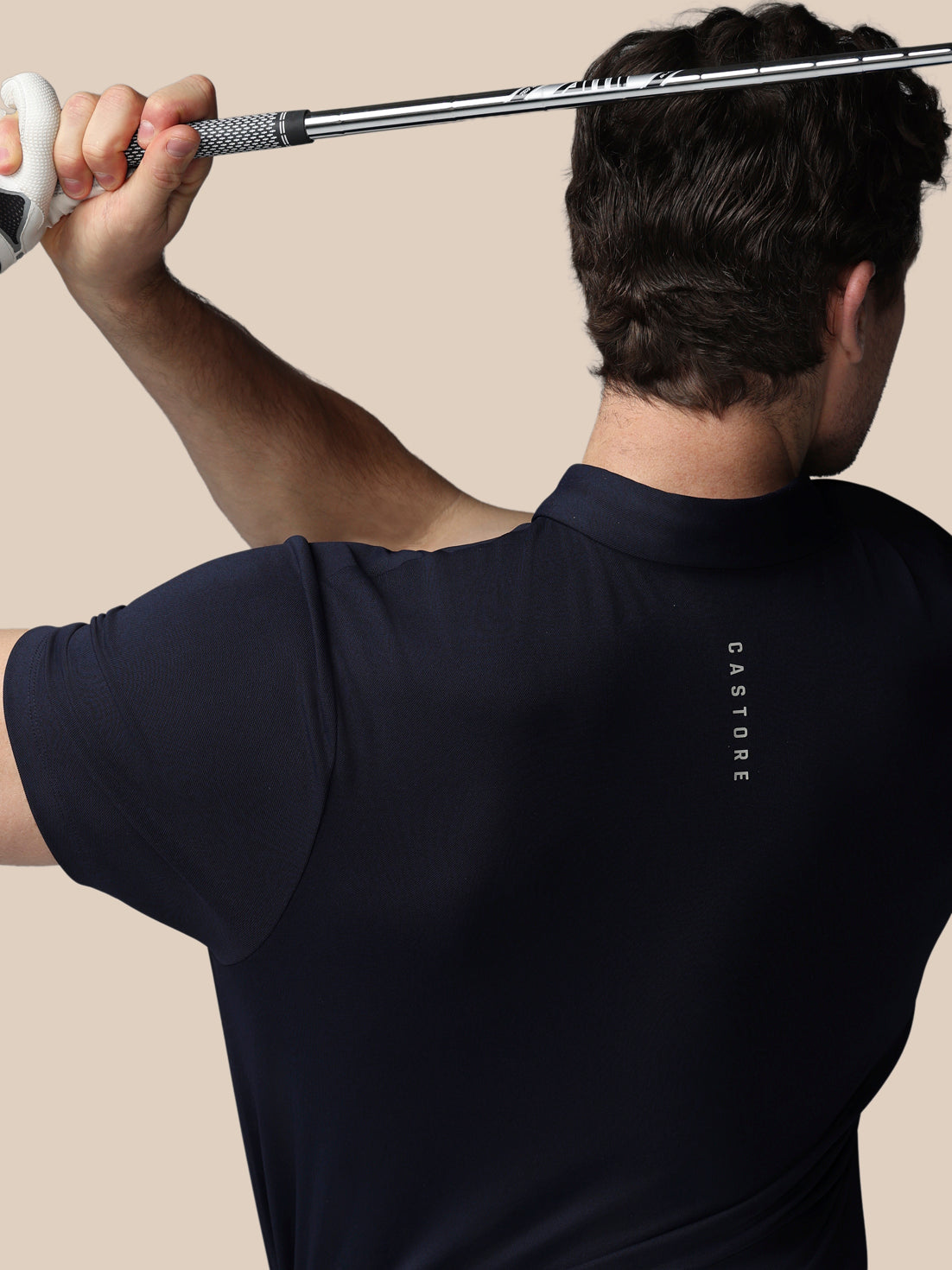 Person wearing a navy blue polo shirt with 'Castore' branding, holding a golf club.