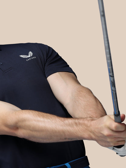 Person wearing a navy blue polo shirt with a logo, holding a golf club against a beige background