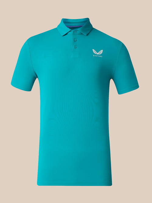 A short-sleeve polo shirt in a vibrant turquoise blue-green color, featuring a white wing logo and the brand name 'CASTORE' on the left chest, displayed on a solid beige background.