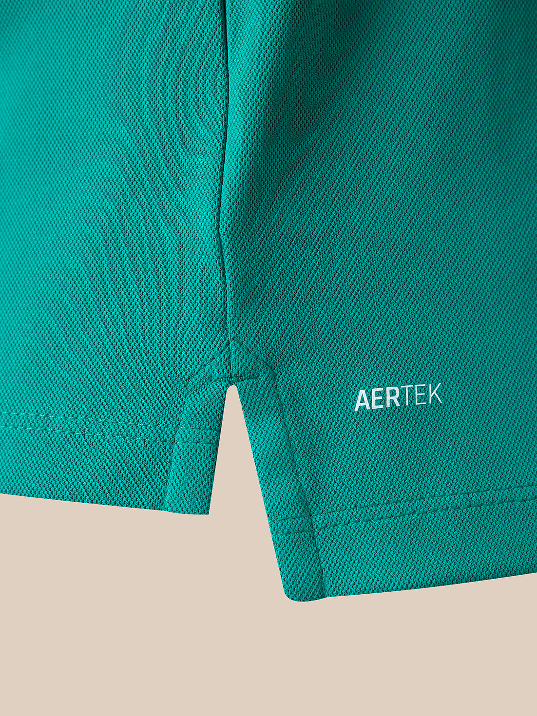 Close-up of a teal-green athletic fabric panel with a small white AERTEK logo near the lower right edge, shown against a light beige background.