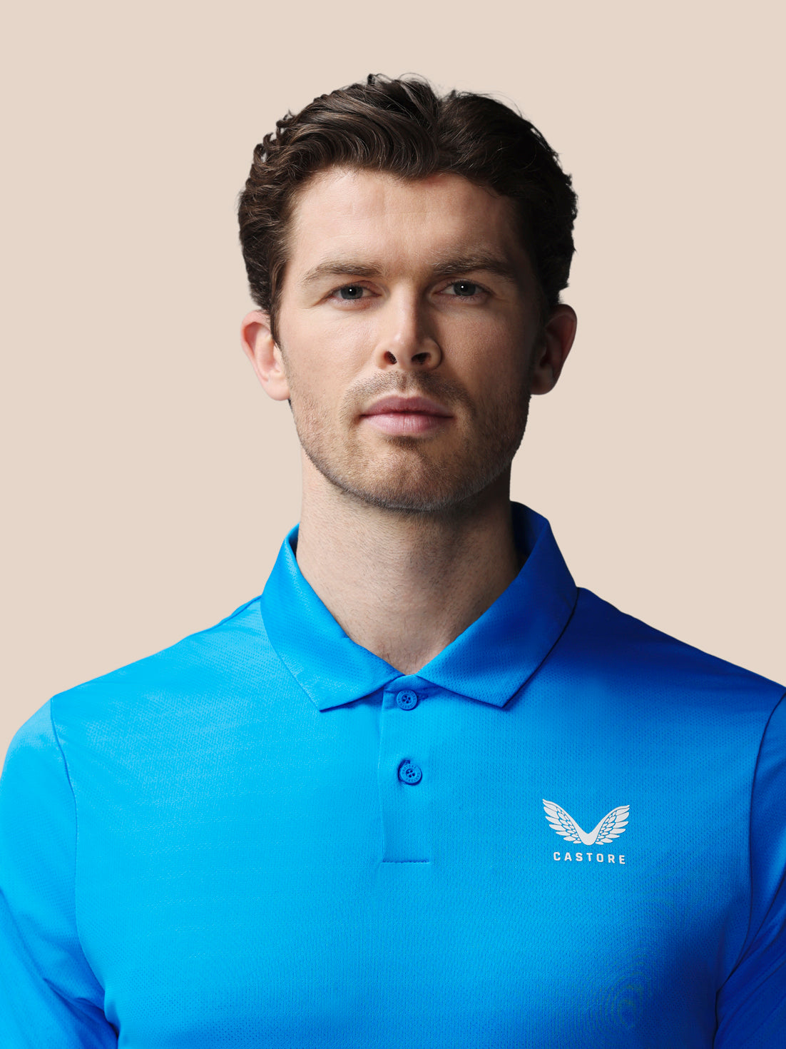 Man wearing a blue polo shirt with a logo on a beige background