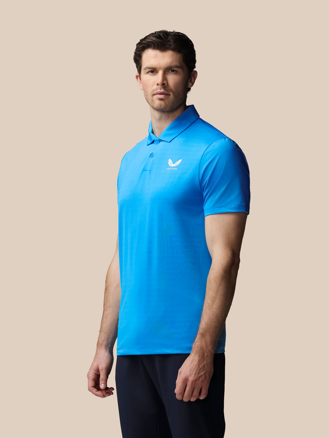 Man wearing a blue polo shirt with a logo on a beige background
