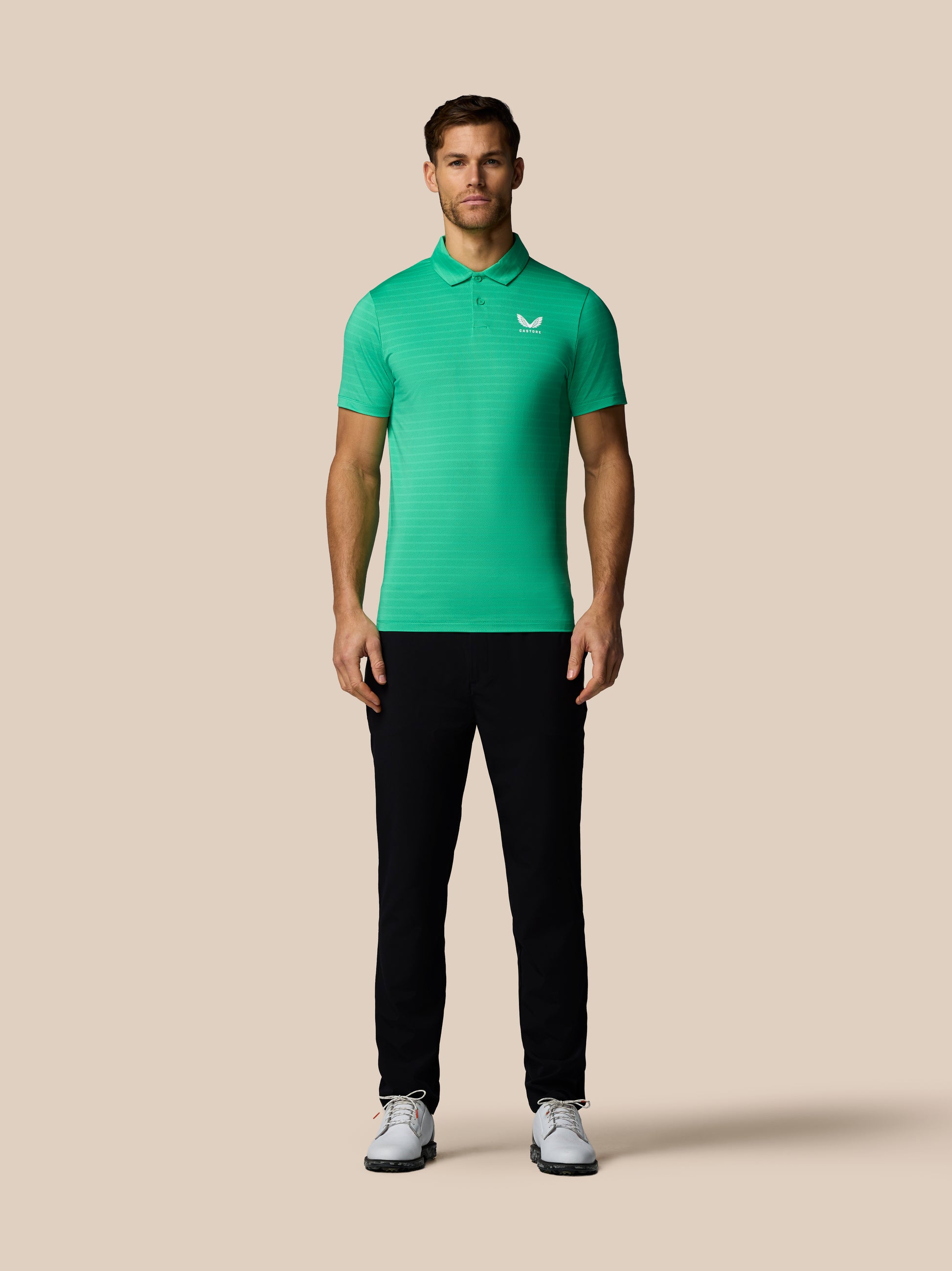 Man wearing a green polo shirt and black pants on a beige background
