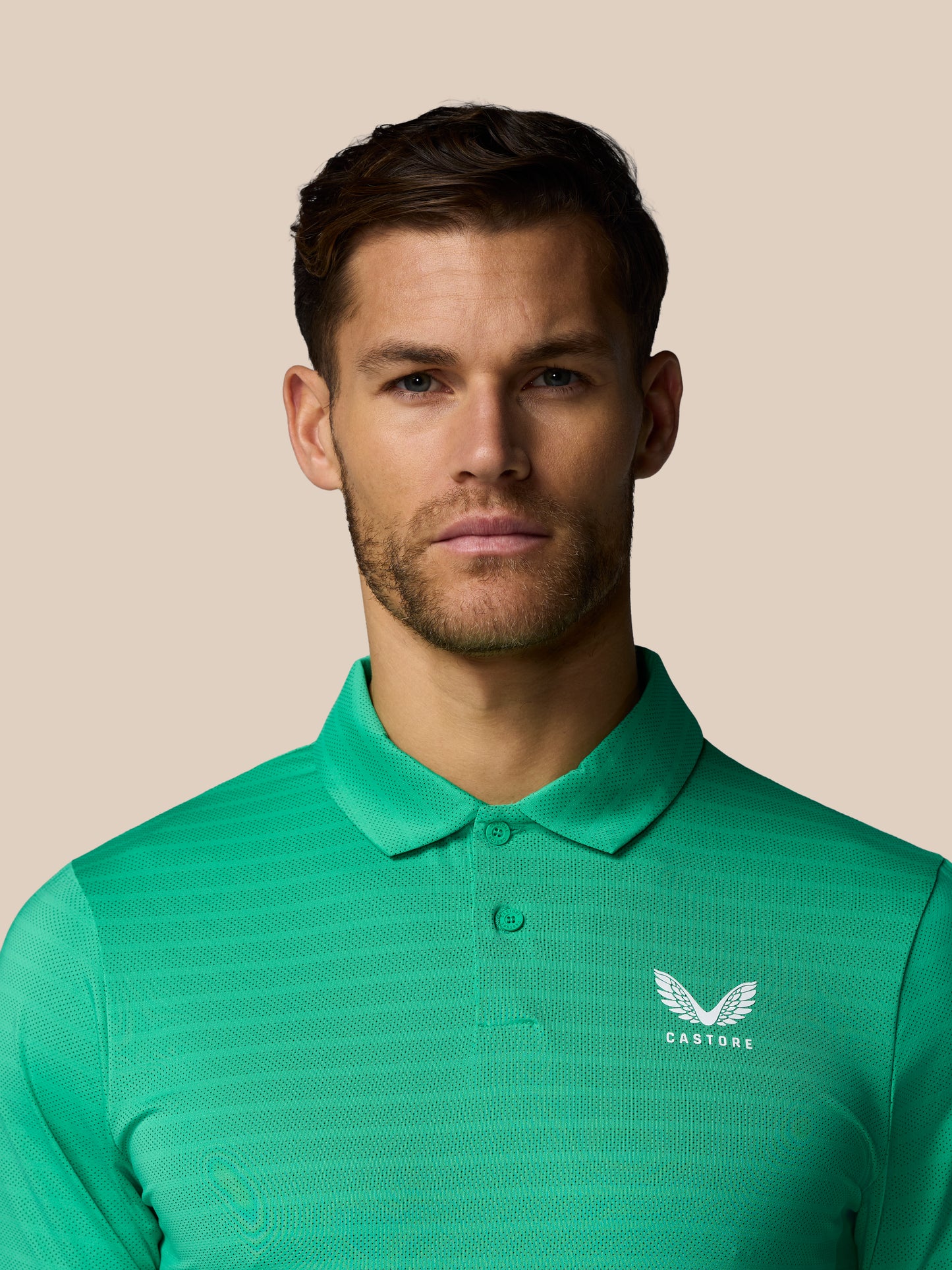 Man wearing a green polo shirt with a Castore logo on a beige background