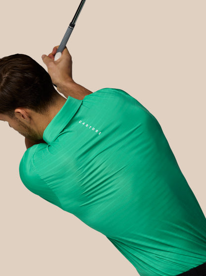 Man in a green shirt swinging a golf club against a beige background