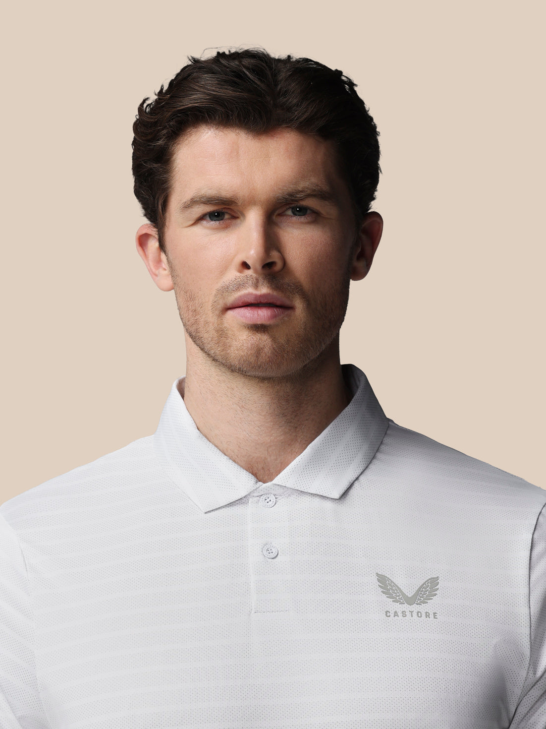 A man wearing a white Castore polo shirt, photographed from the chest up against a solid beige background.