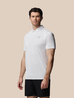 Man wearing a white polo shirt with a logo on a beige background
