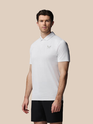 A man wearing a white short-sleeve polo shirt with a small gray embroidered logo on the left chest, paired with black shorts, set against a solid beige background.
