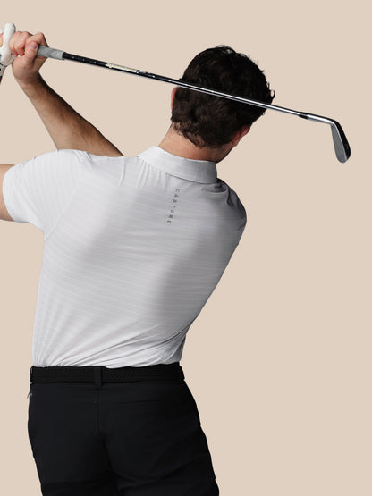 Person in a white shirt and black pants swinging a golf club against a beige background