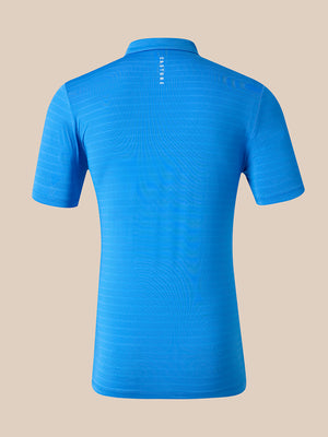 A bright blue short-sleeve athletic polo shirt shown from the back, featuring a subtle wavy texture and a vertical white 'CASTORE' logo printed at the center neck, set against a solid beige background.