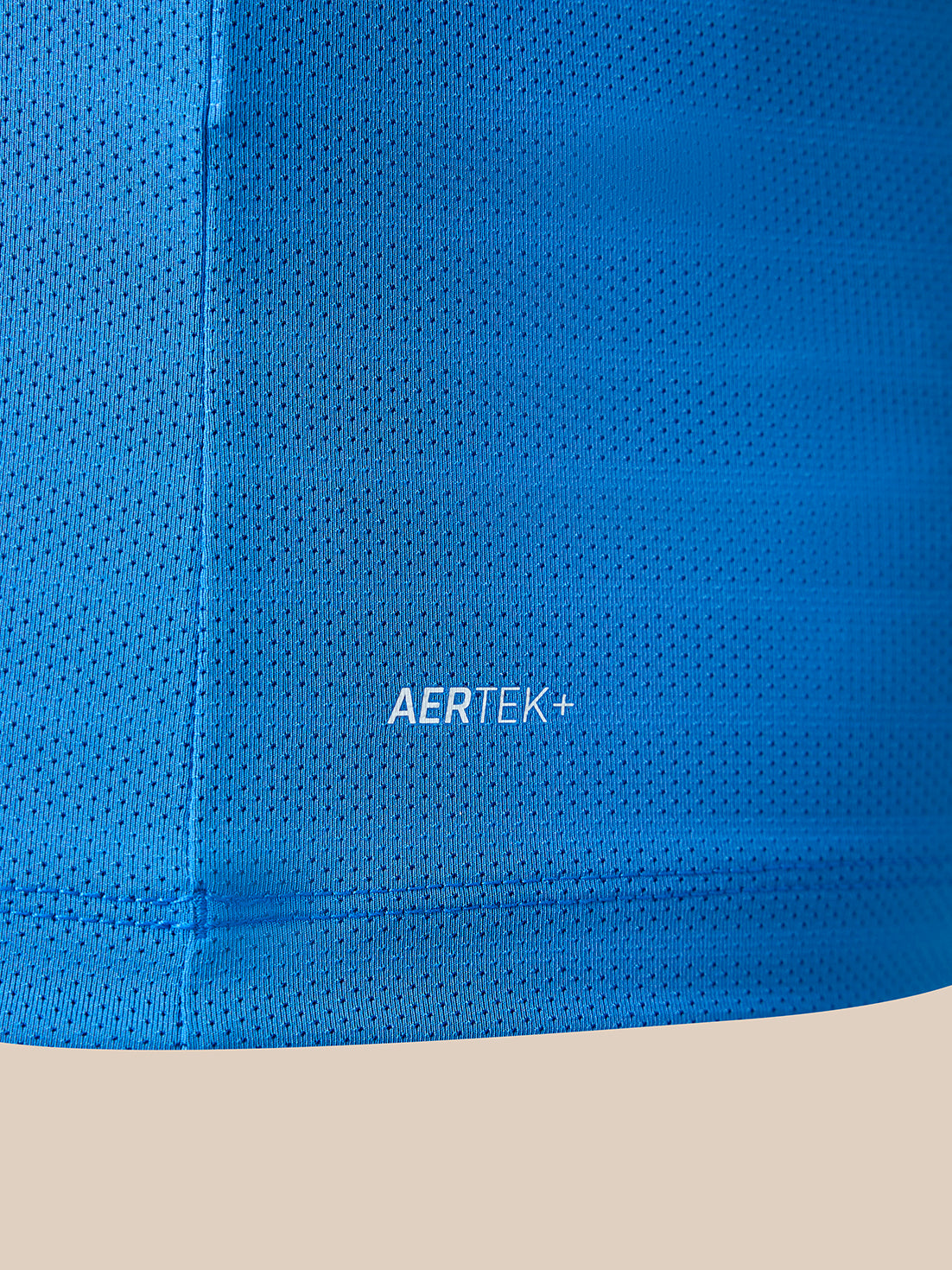 Close-up of a bright blue perforated athletic fabric with the AERTEK+ logo printed in white, set against a light beige background.