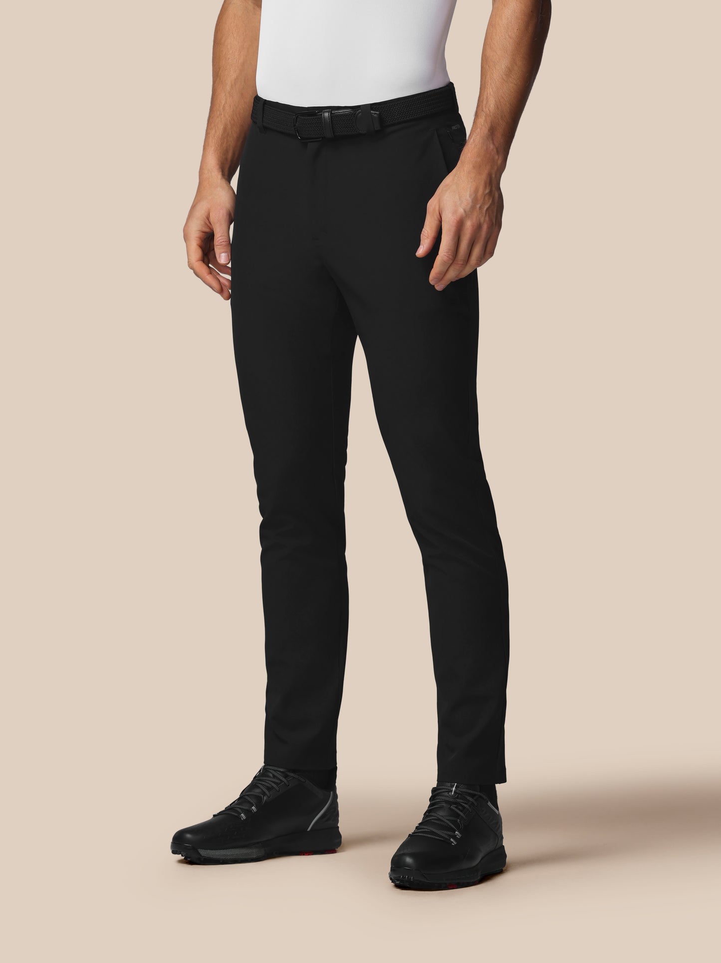 Person wearing black pants and black shoes on a beige background