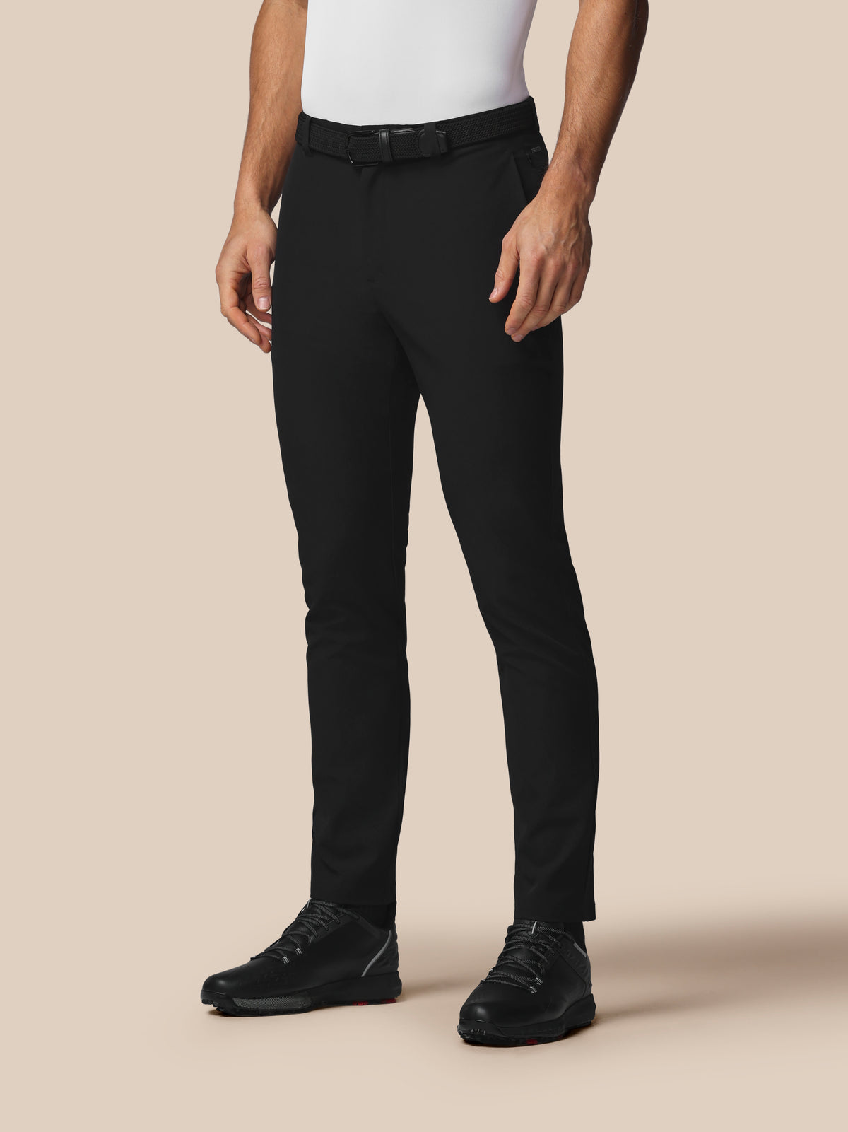 Person wearing black pants and black shoes on a beige background
