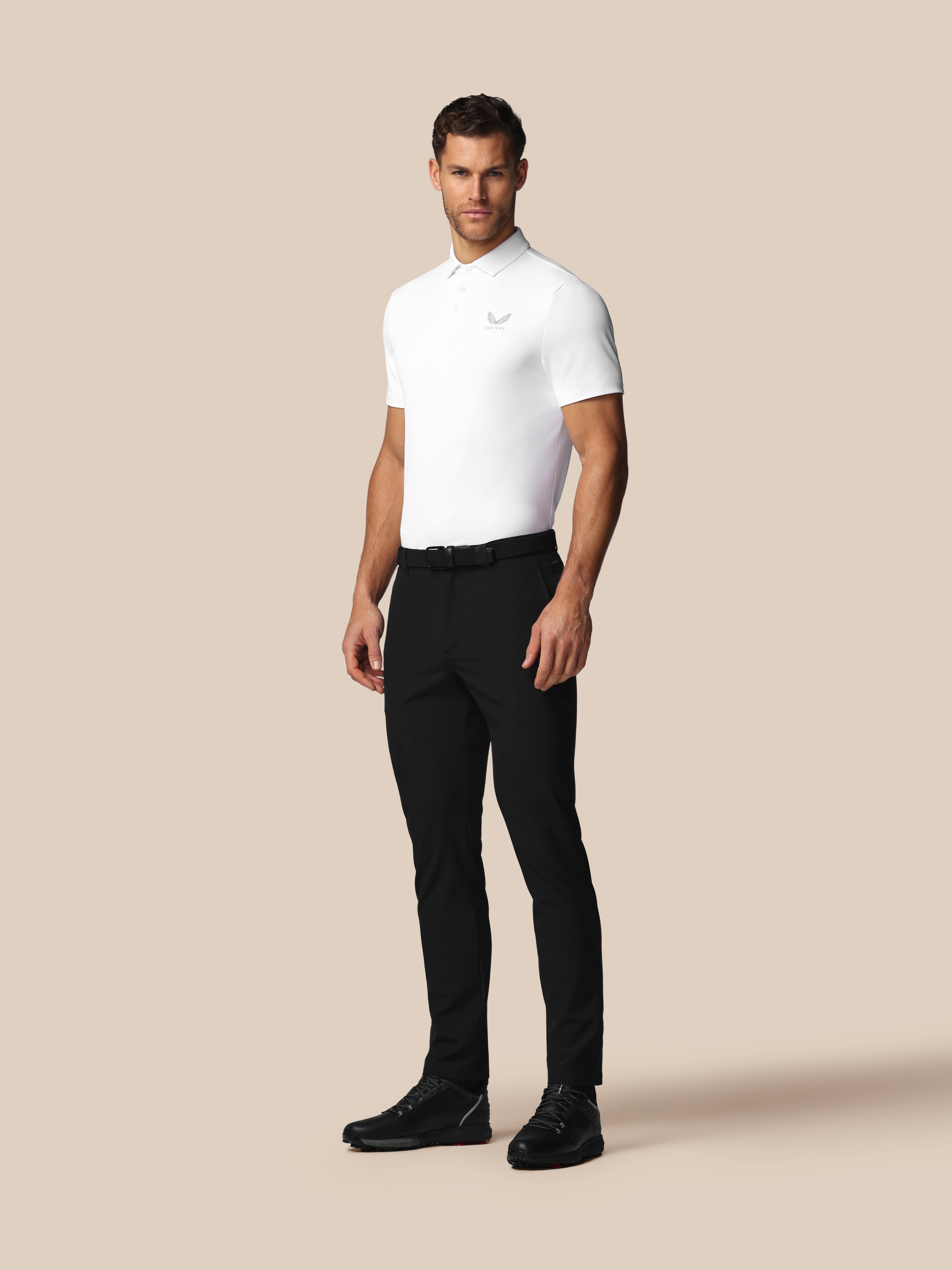 Man wearing a white polo shirt and black pants on a beige background