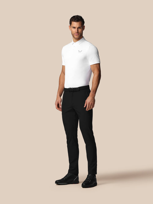 Man wearing a white polo shirt and black pants on a beige background