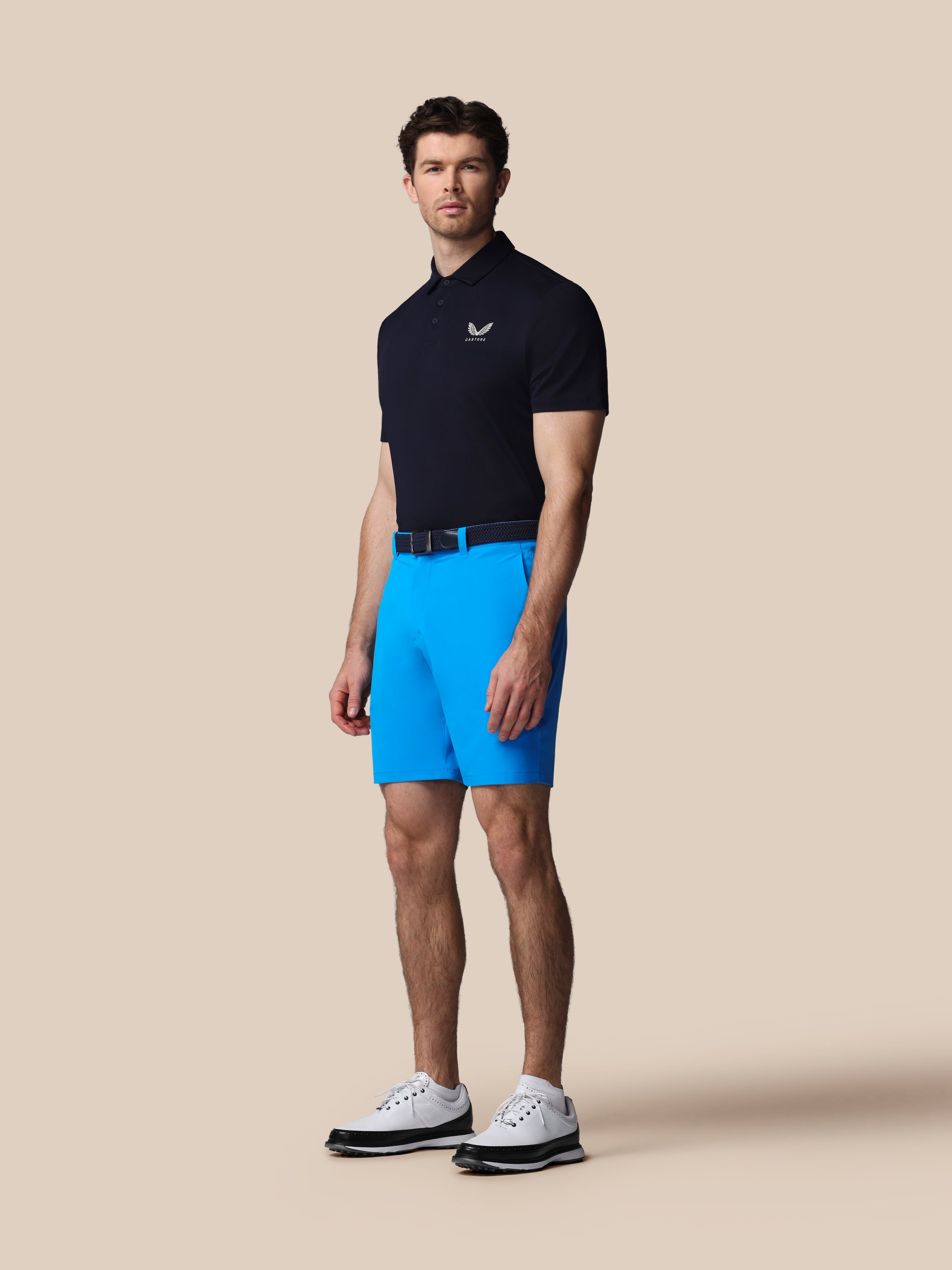 Man wearing a black polo shirt and blue shorts on a beige background