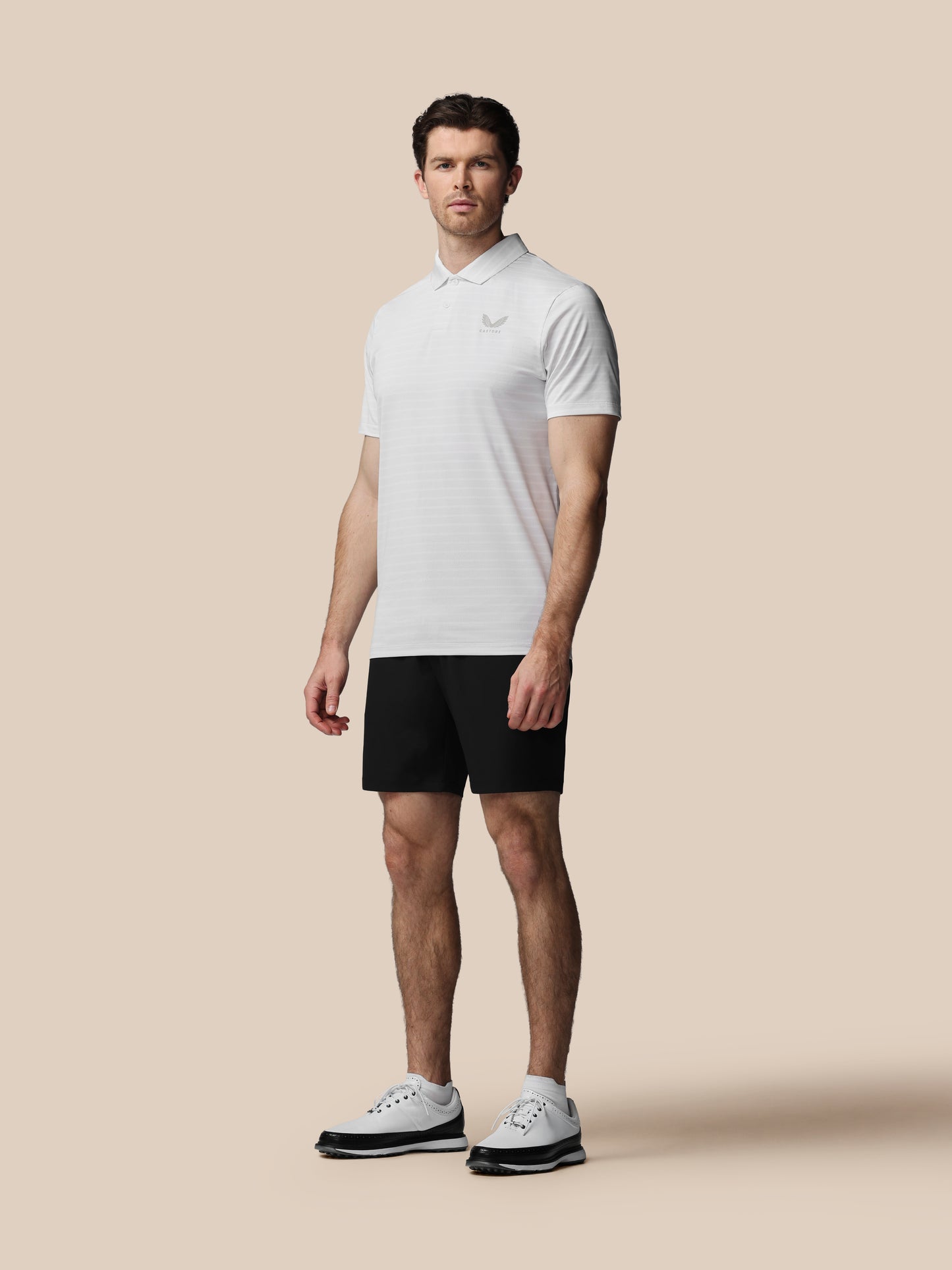 Man wearing a white polo shirt and black shorts on a beige background