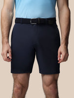 Person wearing navy shorts and a light blue shirt on a beige background