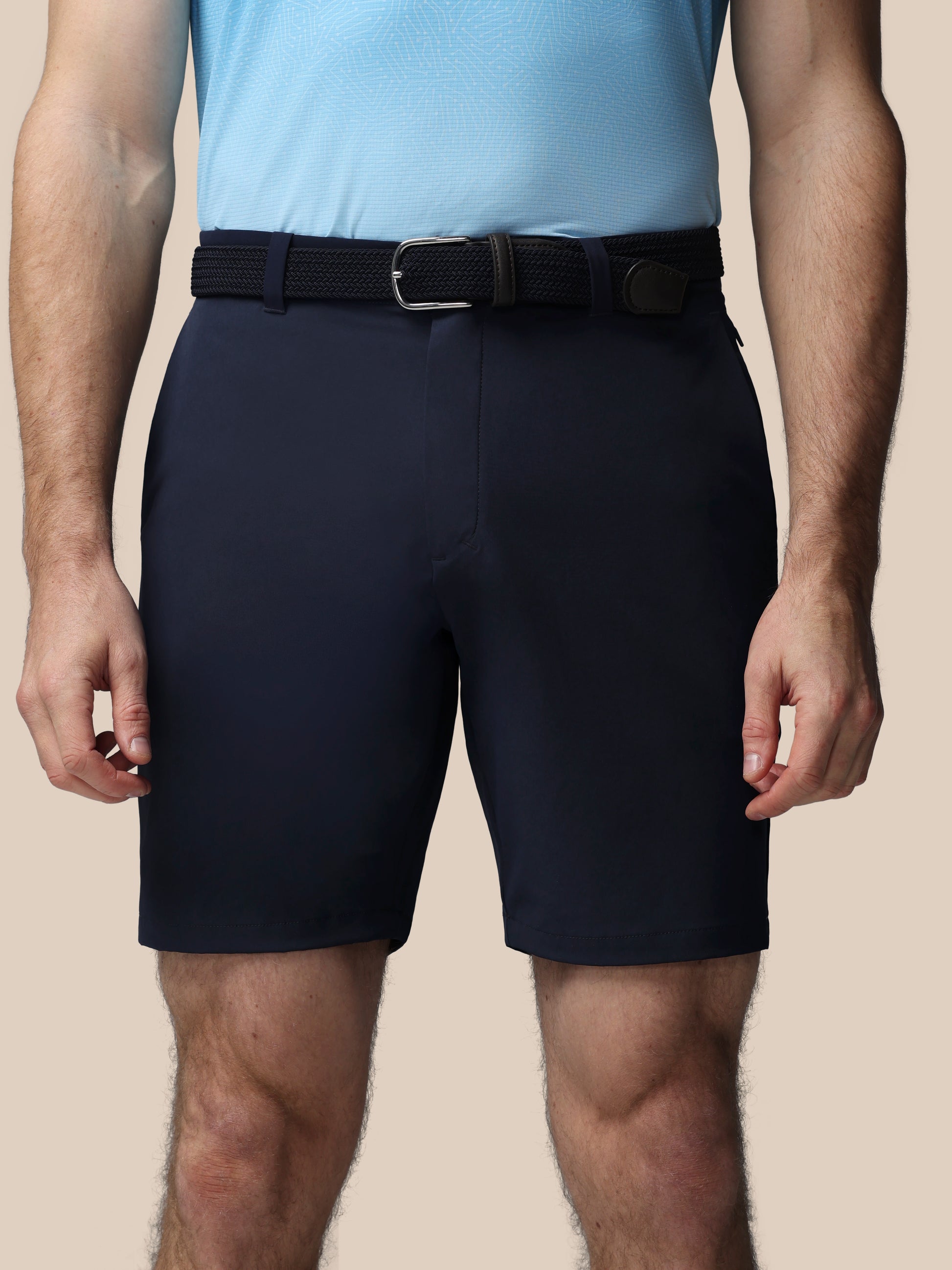 Person wearing navy shorts and a light blue shirt on a beige background