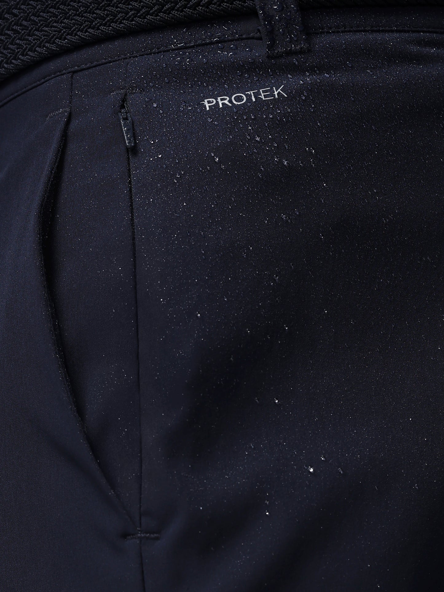 Close-up of navy pants with 'PROTEK' branding on a dark background