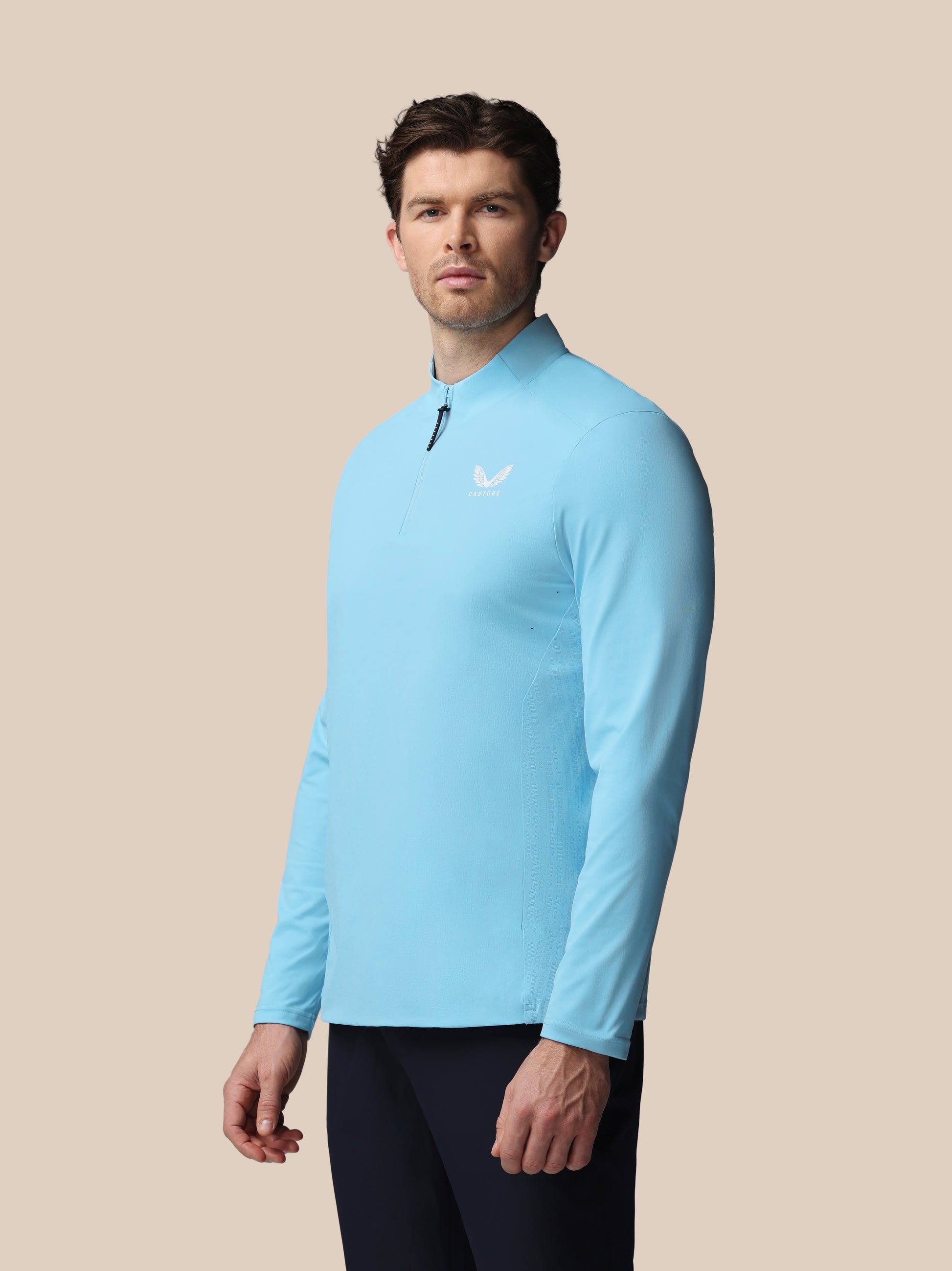 Man wearing a light blue long-sleeve shirt with a logo on a beige background