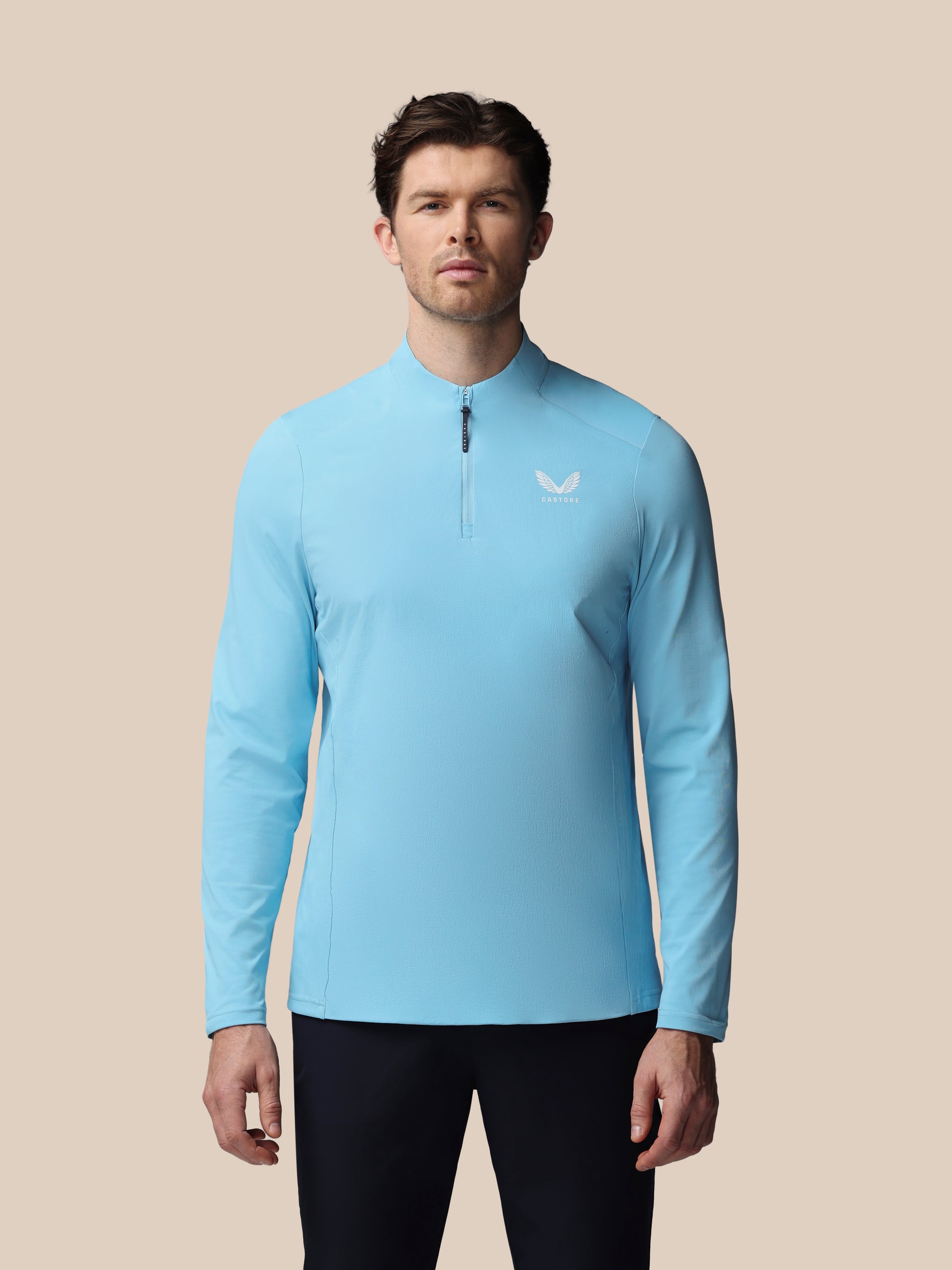 Man wearing a light blue long-sleeve athletic shirt with a logo on a beige background