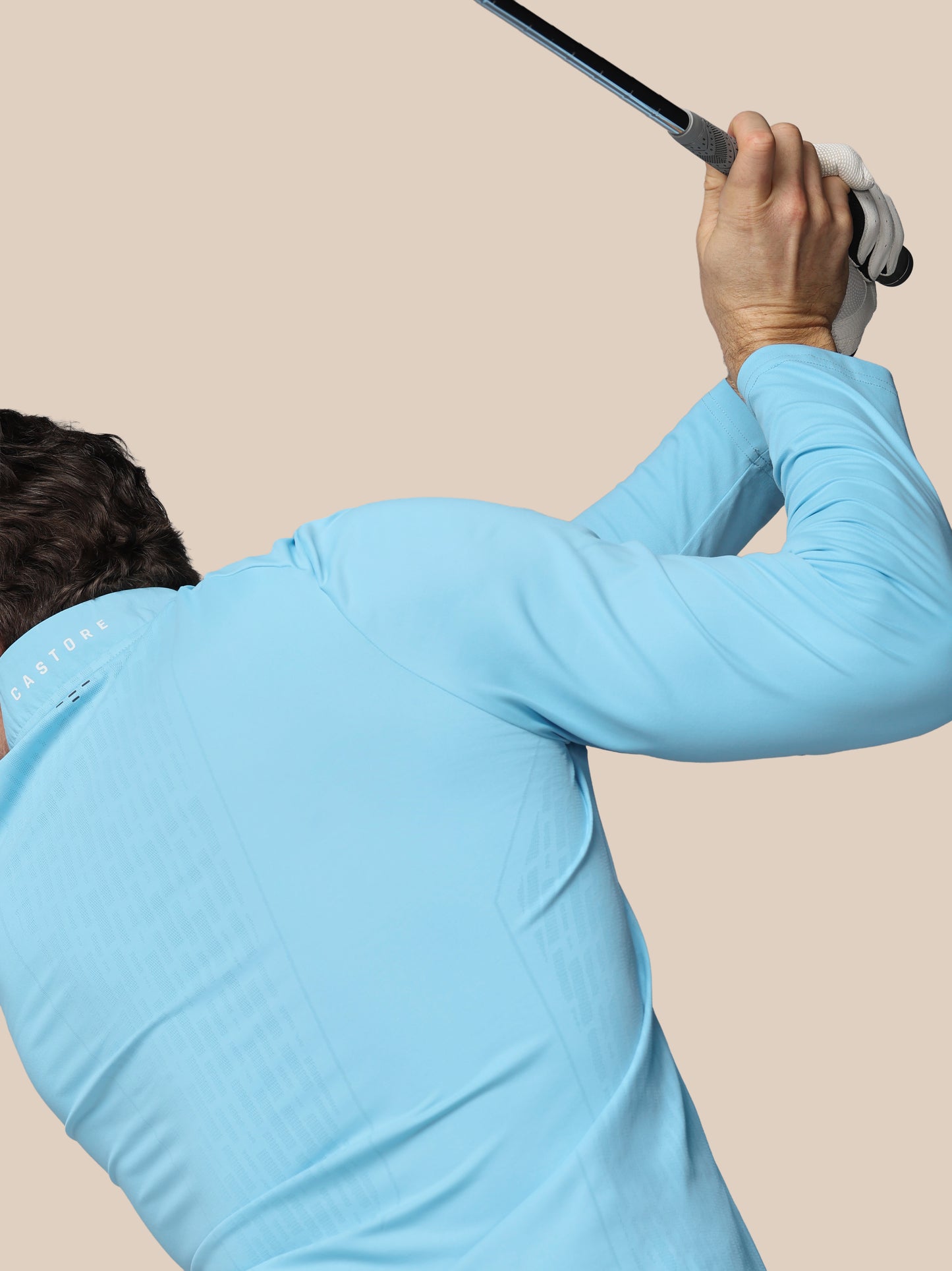 Person in light blue shirt holding a golf club against a beige background