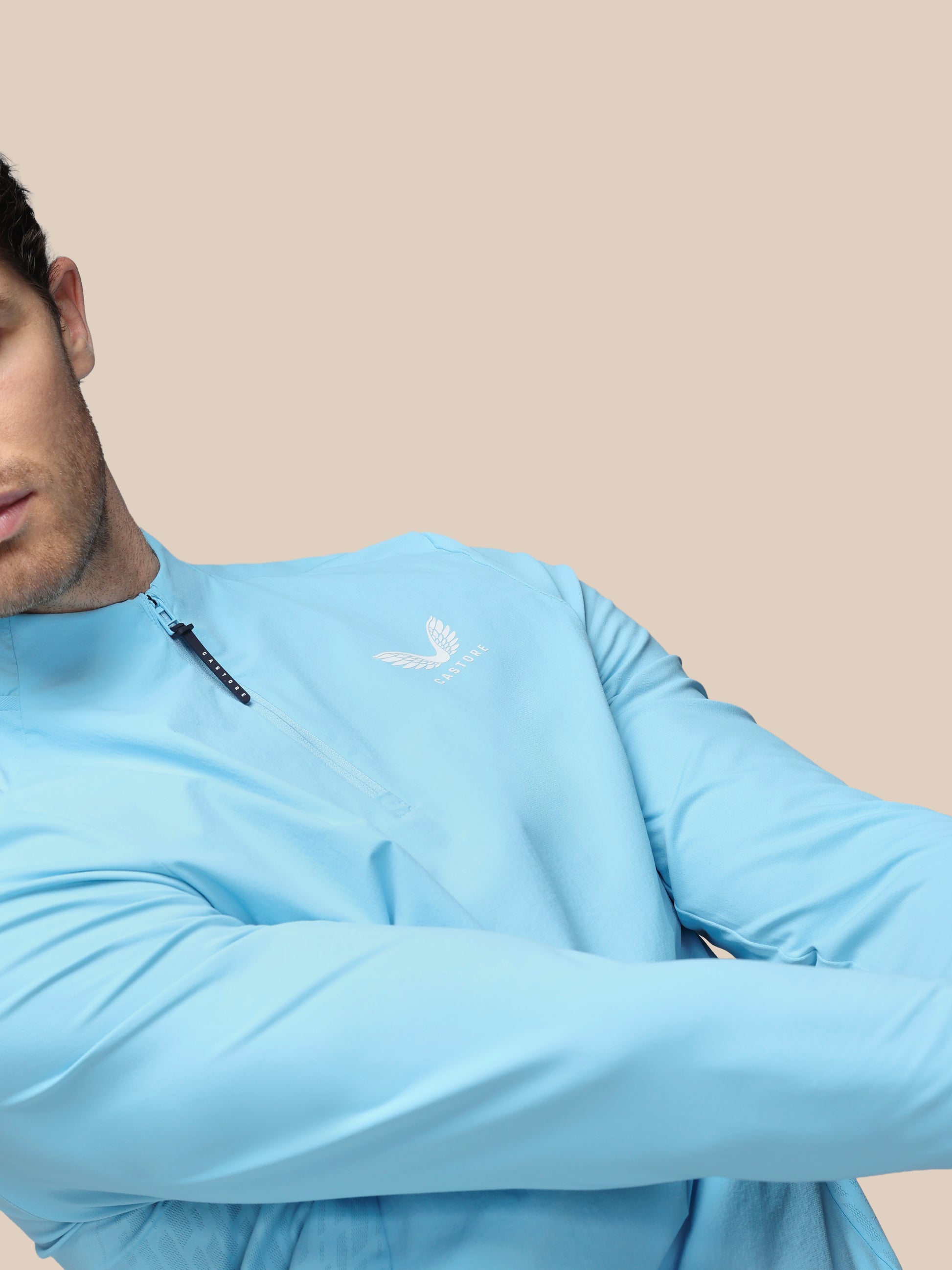 Person wearing a light blue long-sleeve shirt with a logo on a beige background