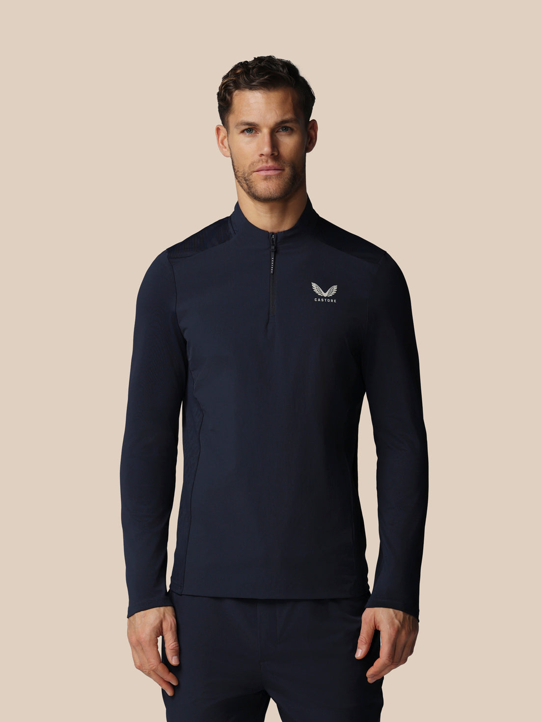 Man wearing a navy long-sleeve athletic shirt with Castore logo on a beige background