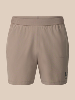 A pair of women's athletic shorts in a solid taupe color, featuring a wide elastic waistband with subtle branding and a small dark logo on the lower left leg, shown against a solid beige background.