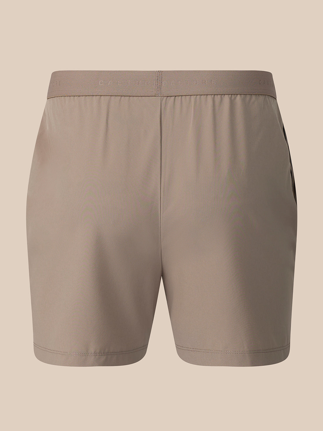 A pair of athletic shorts in a solid taupe color, shown from the back against a solid beige background.