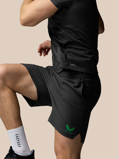 Person wearing black athletic shorts with a green logo on a beige background