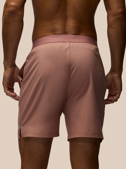 Rear view of a man wearing dusty rose athletic shorts against a solid beige background.