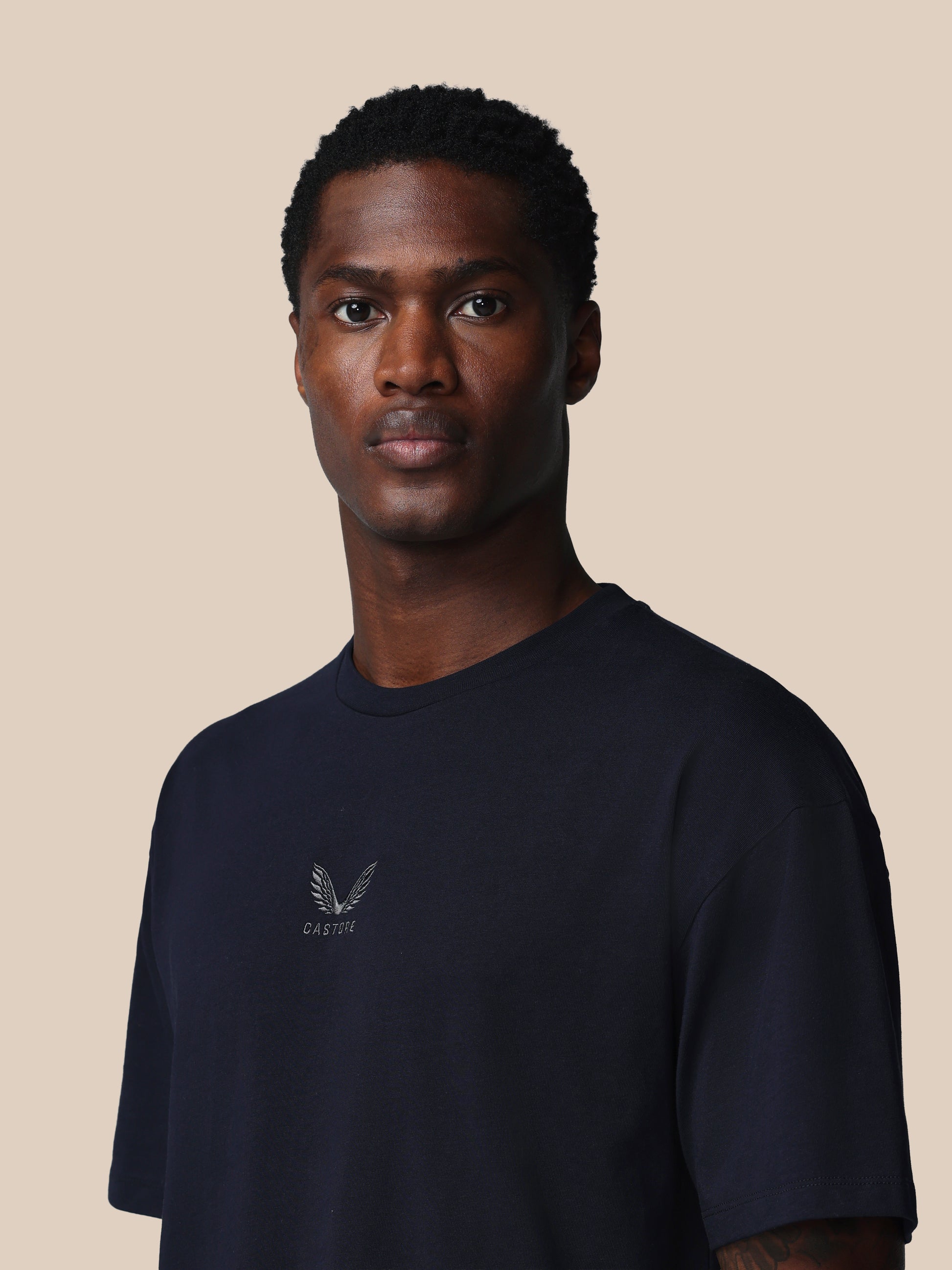 Man wearing a navy blue t-shirt with a logo on a beige background