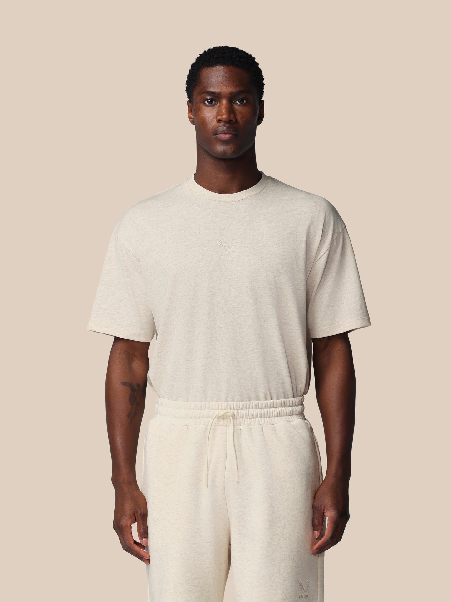 Man wearing a beige t-shirt and pants against a beige background