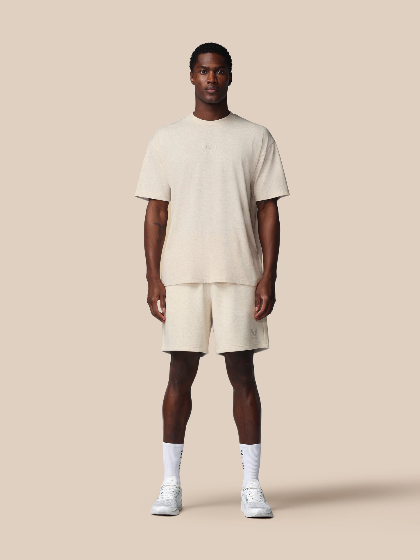 Man wearing a beige t-shirt and shorts set on a plain background